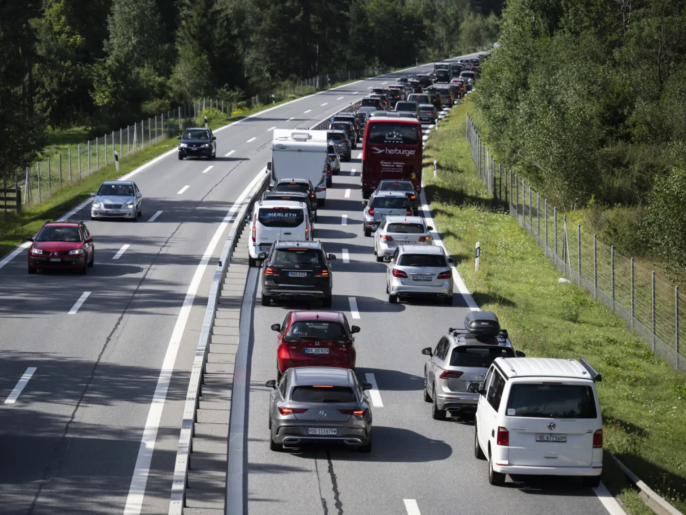 Traffico intenso su un'autostrada con diverse auto ferme e in movimento. Lungo la carreggiata si osservano alberi verdi ai lati.