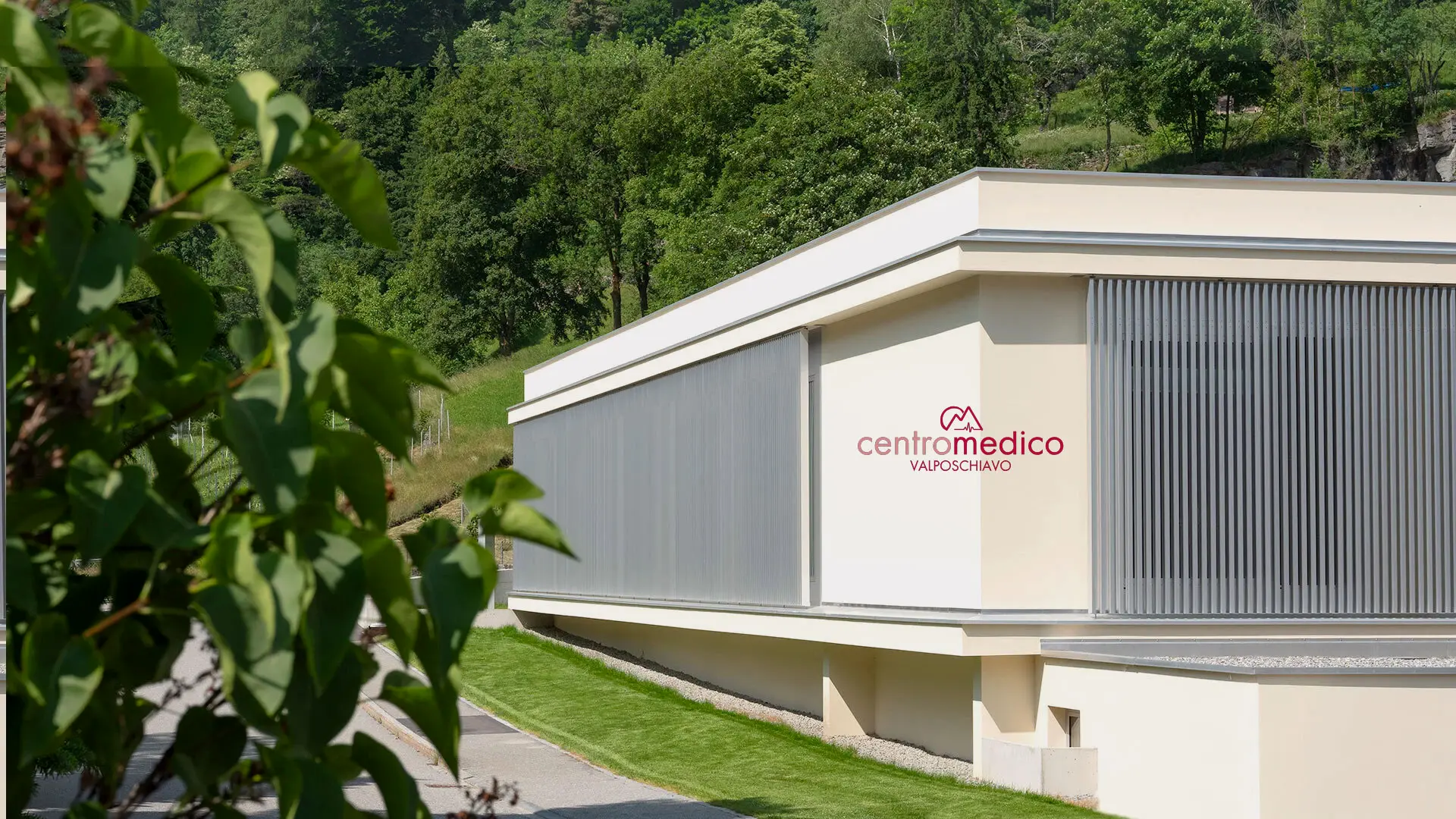 Facciata moderna del Centro Medico Valtorviano, con pareti chiare e ampie finestre schermate. Ulivi e verde circostante creano un'atmosfera tranquilla.