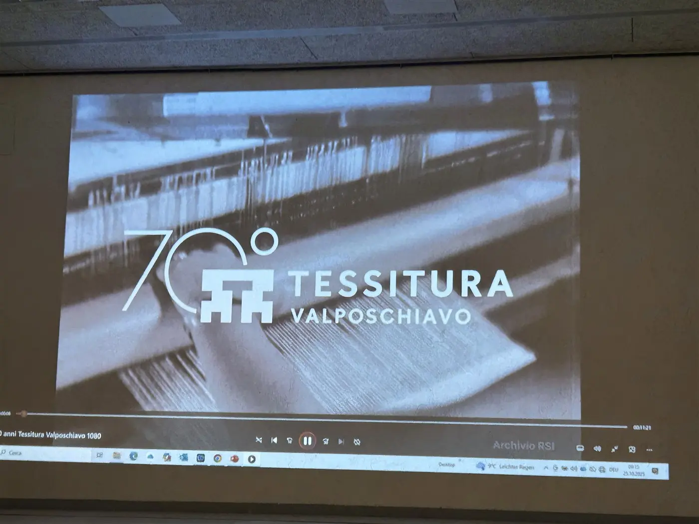 Logo della Tessitura Valposchiavo con il numero 70, su uno sfondo di tessuti e telai in bianco e nero.