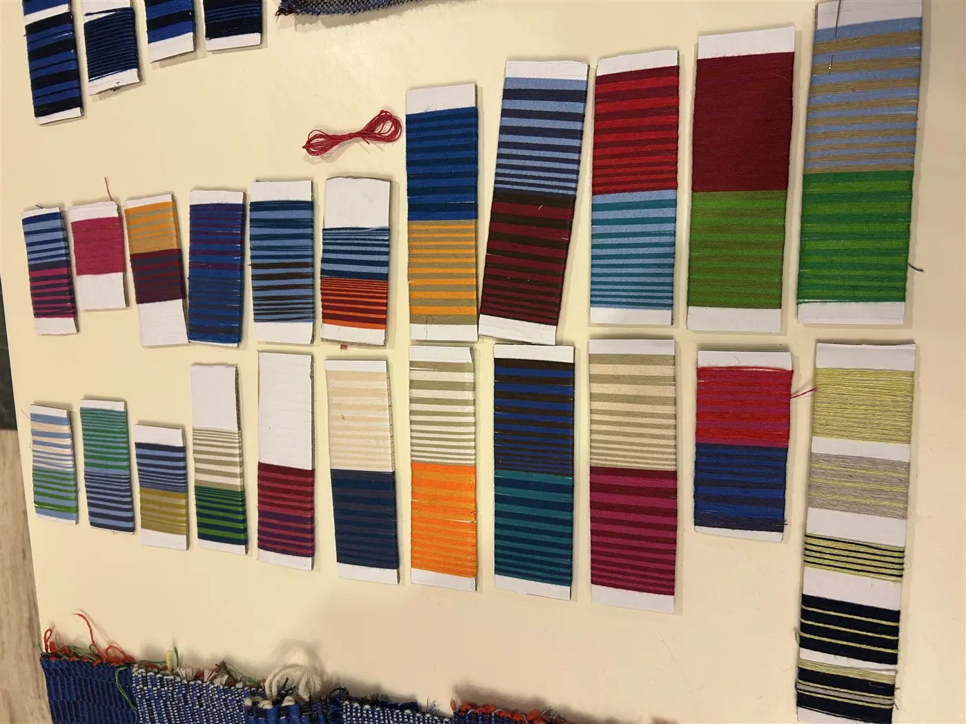 Strisce di tessuto multicolore disposte su un tavolo. Ogni striscia presenta una combinazione di colori e motivi, con tonalità come blu, verde, arancione e rosso.