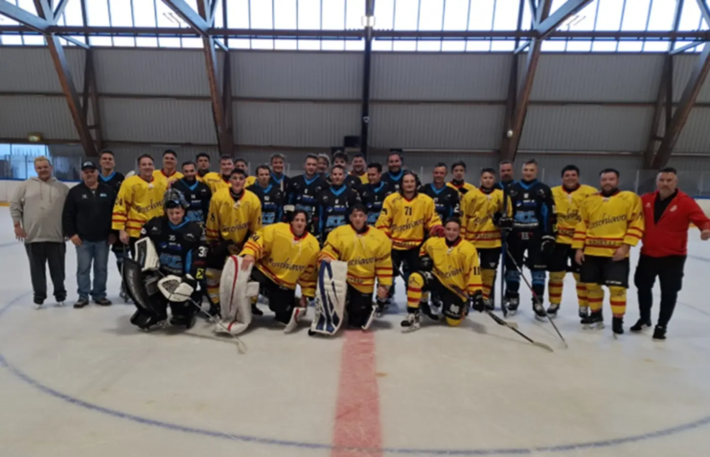 Gruppo di giocatori di hockey su ghiaccio in divise gialle e blu, posano insieme sul ghiaccio. Sullo sfondo, la struttura della pista di ghiaccio.