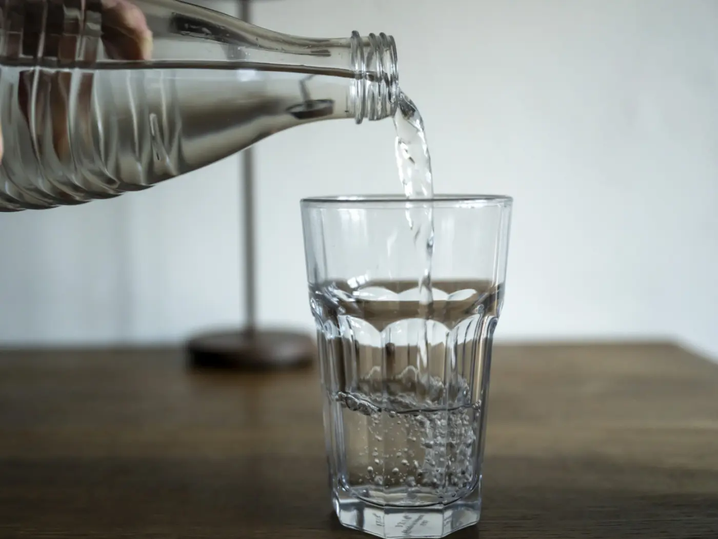 Acqua versata da una bottiglia in un bicchiere su un tavolo di legno. Si vedono bolle d'aria nell'acqua mentre riempie il bicchiere