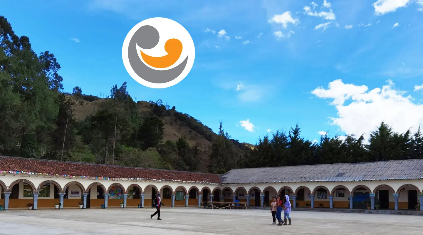 Corte centrale con archi bianchi e un cielo blu chiaro. Persone camminano sul pavimento in cemento. Sullo sfondo si vedono alberi e colline. Un