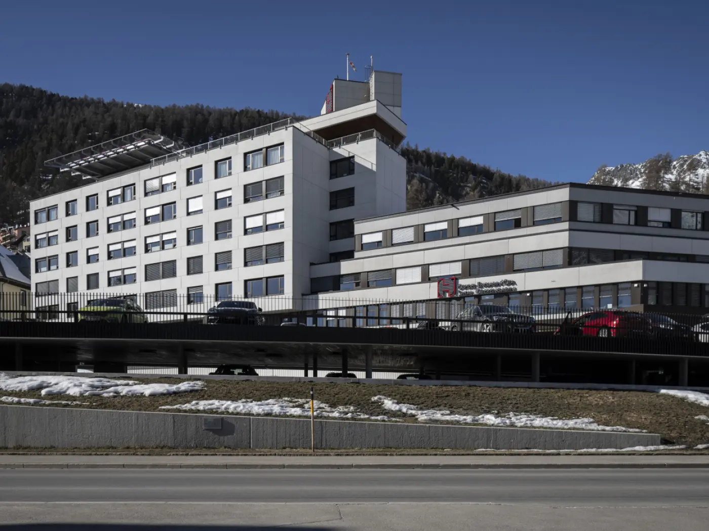 Edificio moderno a più piani con design contemporaneo, situato in un'area montana. La facciata presenta grandi finestre e un tetto con pannelli solari. Str