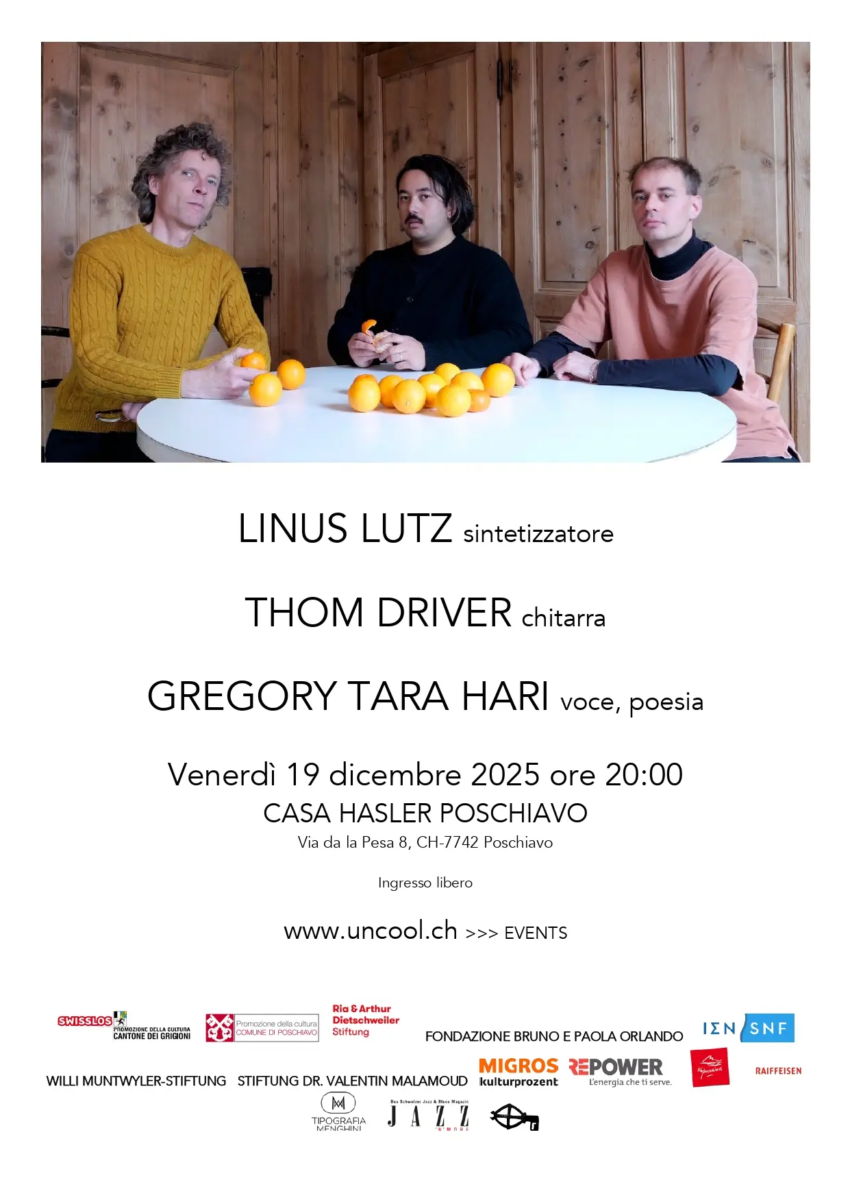 Tre musicisti seduti attorno a un tavolo, sorridenti, con strumenti musicali. Sul tavolo è presente un sintetizzatore e una chitarra. In primo piano i nom