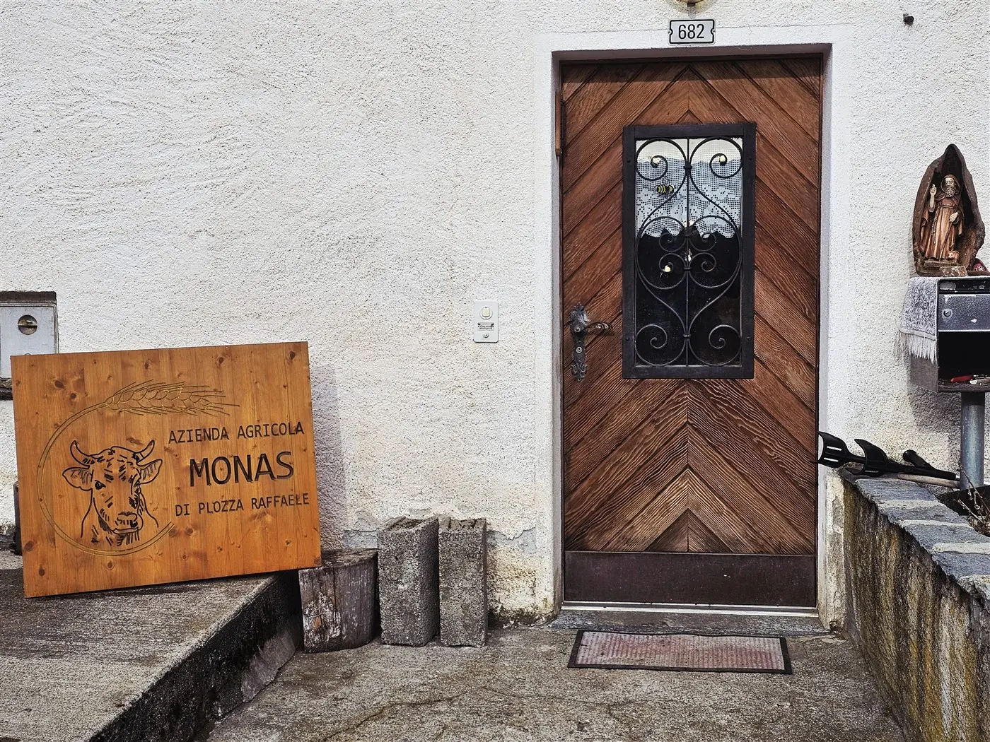 Porta in legno con dettagli a zig-zag, accanto a un'insegna di legno che riporta "Azienda Agricola Monas di Piozza Raffaele