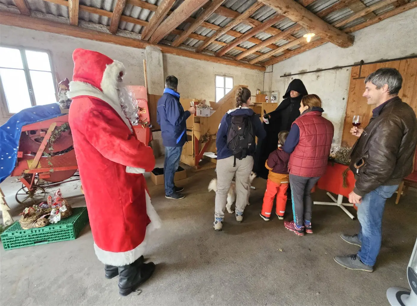 Un gruppo di persone in un ambiente interno decorato per il Natale. Un uomo vestito da Babbo Natale si trova a sinistra, mentre gli altri interagiscono e osservano decorazioni.