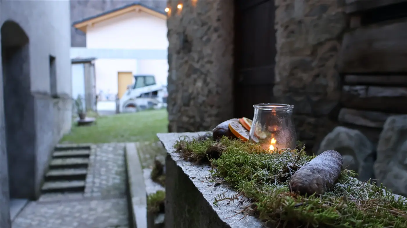 Una strada stretta in un vicolo con erba e muschio sul bordo. Un barattolo di vetro con una candela accesa illumina la scena. In primo piano ci sono