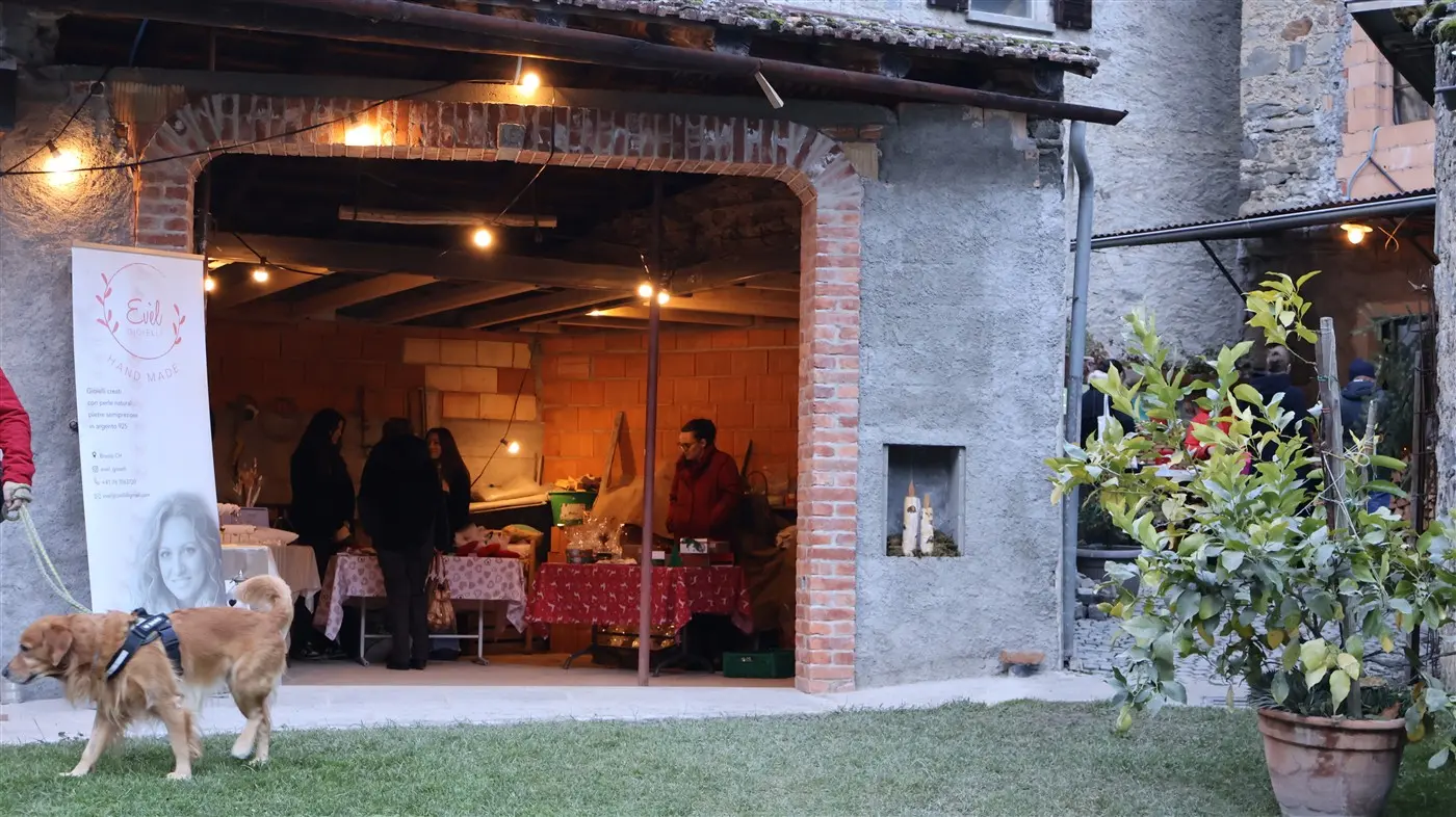 Un'atmosfera accogliente con un mercato all'aperto. All'interno di un edificio in pietra, alcune persone chiacchierano mentre sono esposte varie merci su tavoli
