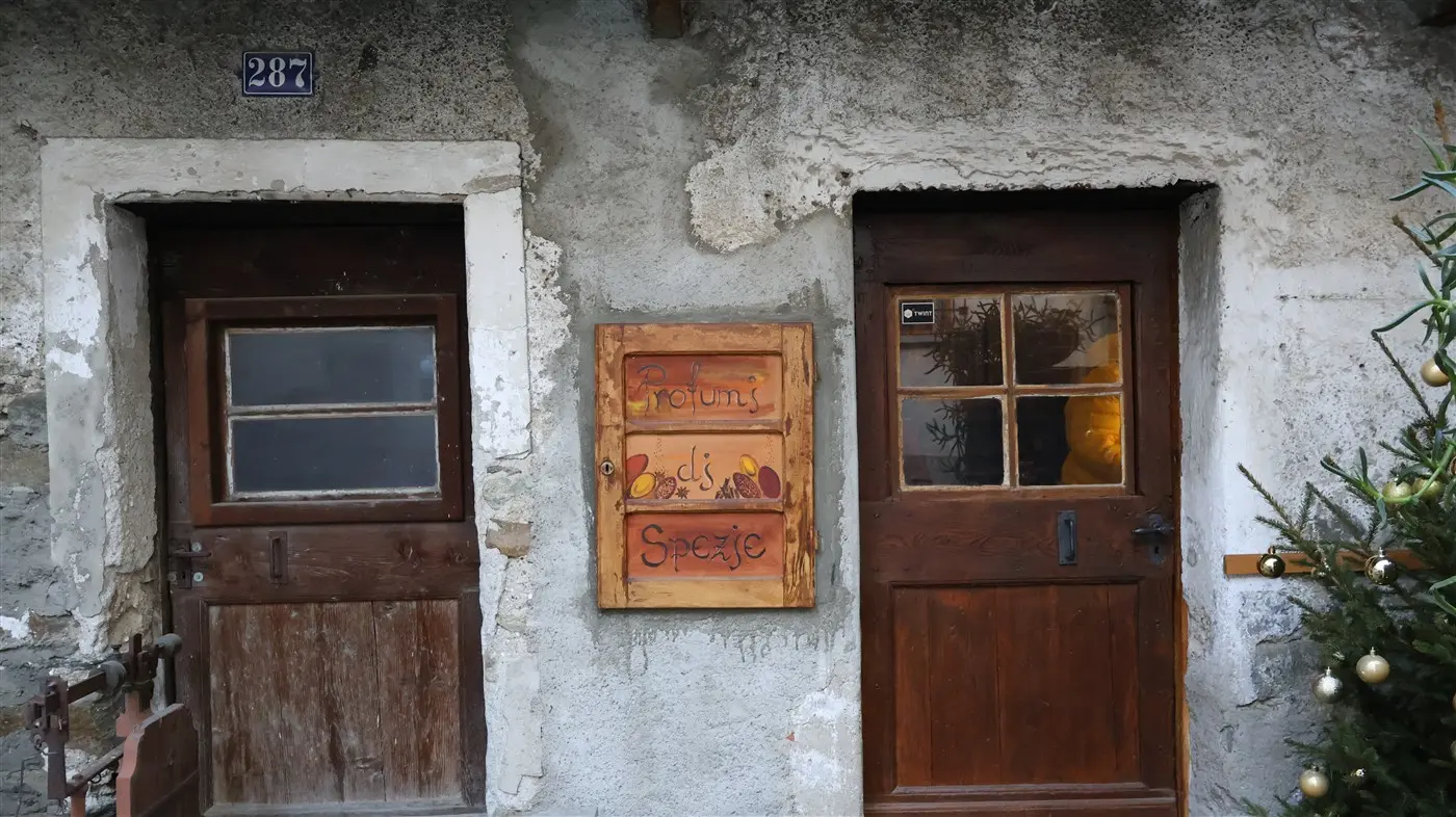 Facciata di un antico edificio con due porte di legno, una a sinistra e l'altra a destra. Tra le porte, un'insegna in legno con la scritta