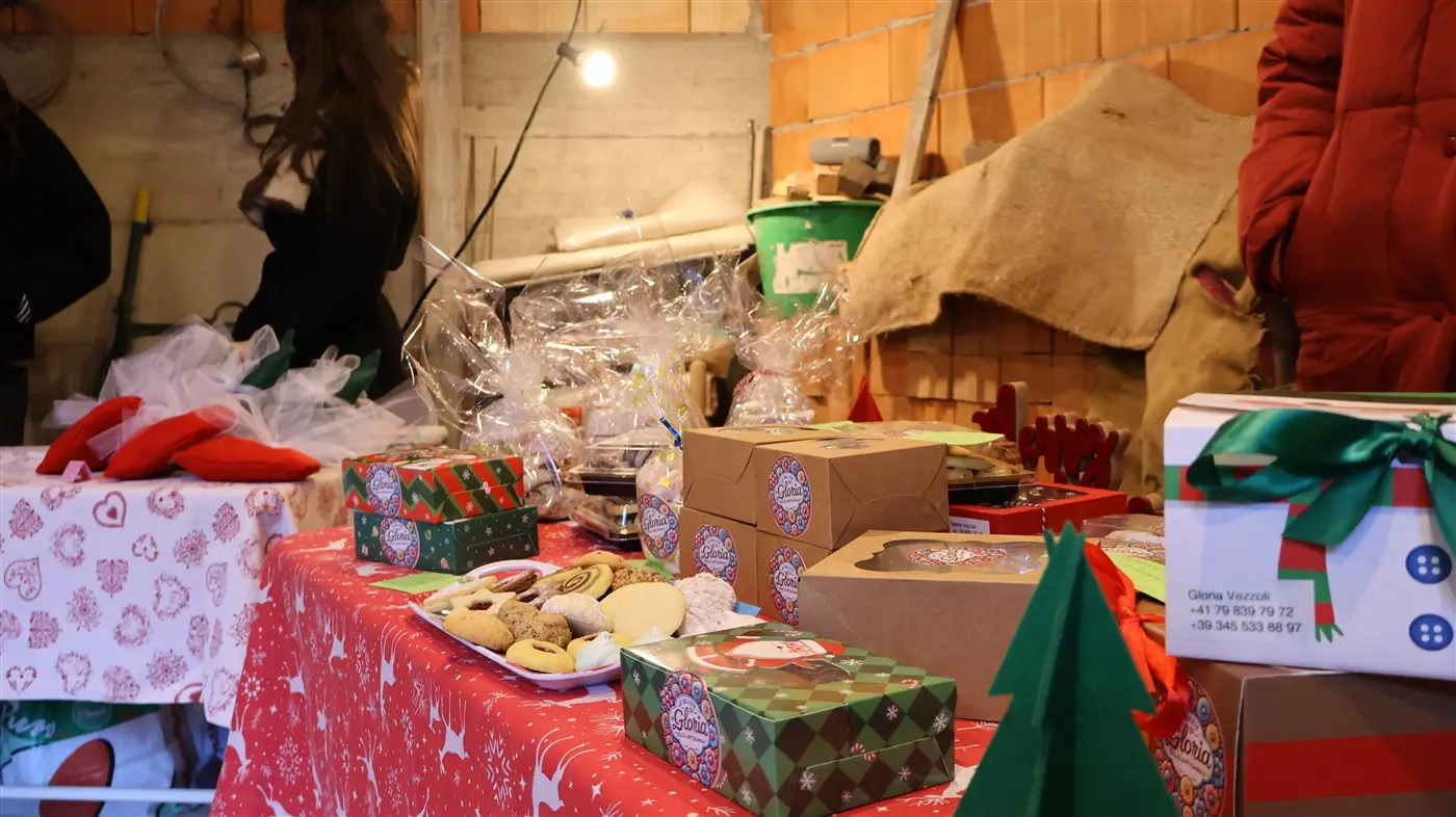 Un bancone decorato con una tovaglia rossa e bianca, adornato con dolci natalizi, biscotti e regalini incartati. Sullo sfondo, oggetti di