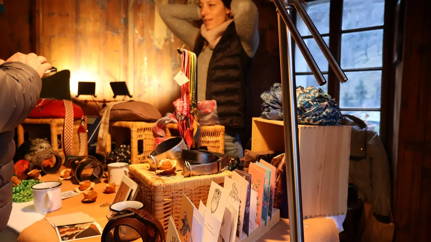 Una donna si sistema i capelli mentre si trova in un ambiente accogliente e luminoso. Sul tavolo ci sono diversi oggetti artigianali, tra cui gioielli, accessori