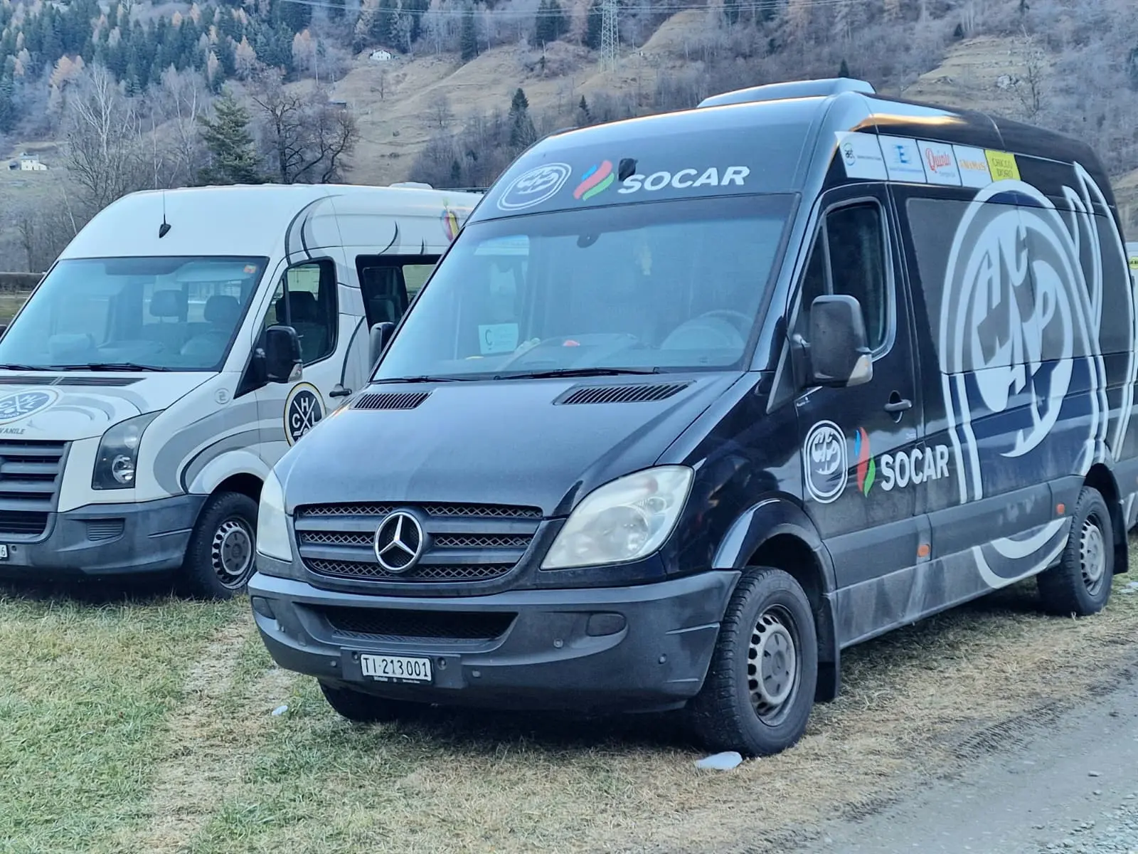 Furgone Mercedes nero con logo Socar parcheggiato accanto a un furgone bianco. Sullo sfondo, colline alberate.