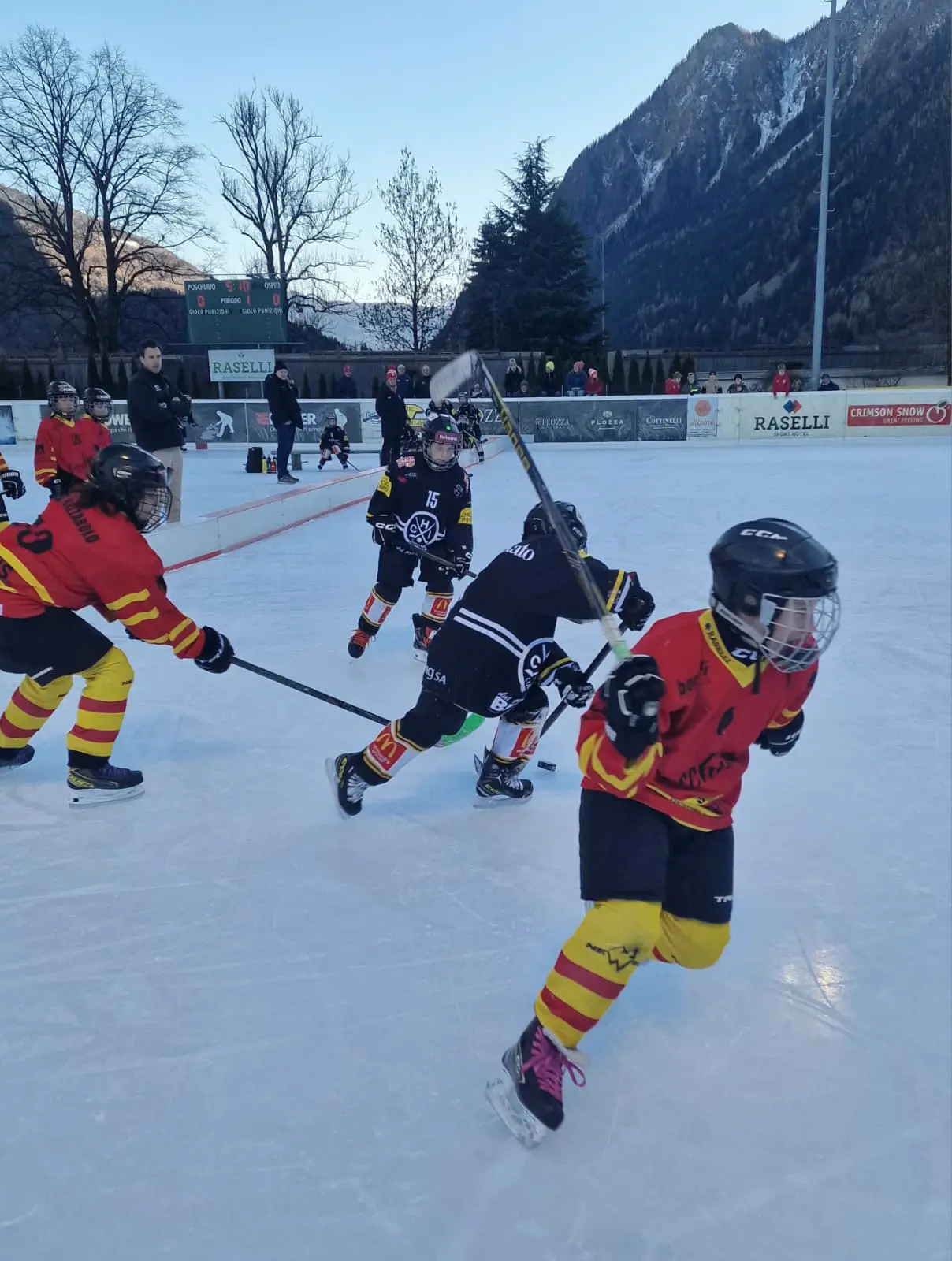 Giocatori di hockey su ghiaccio in azione sul campo. Due bambini indossano maglie rosse e gialle, mentre uno in maglia nera si muove con una