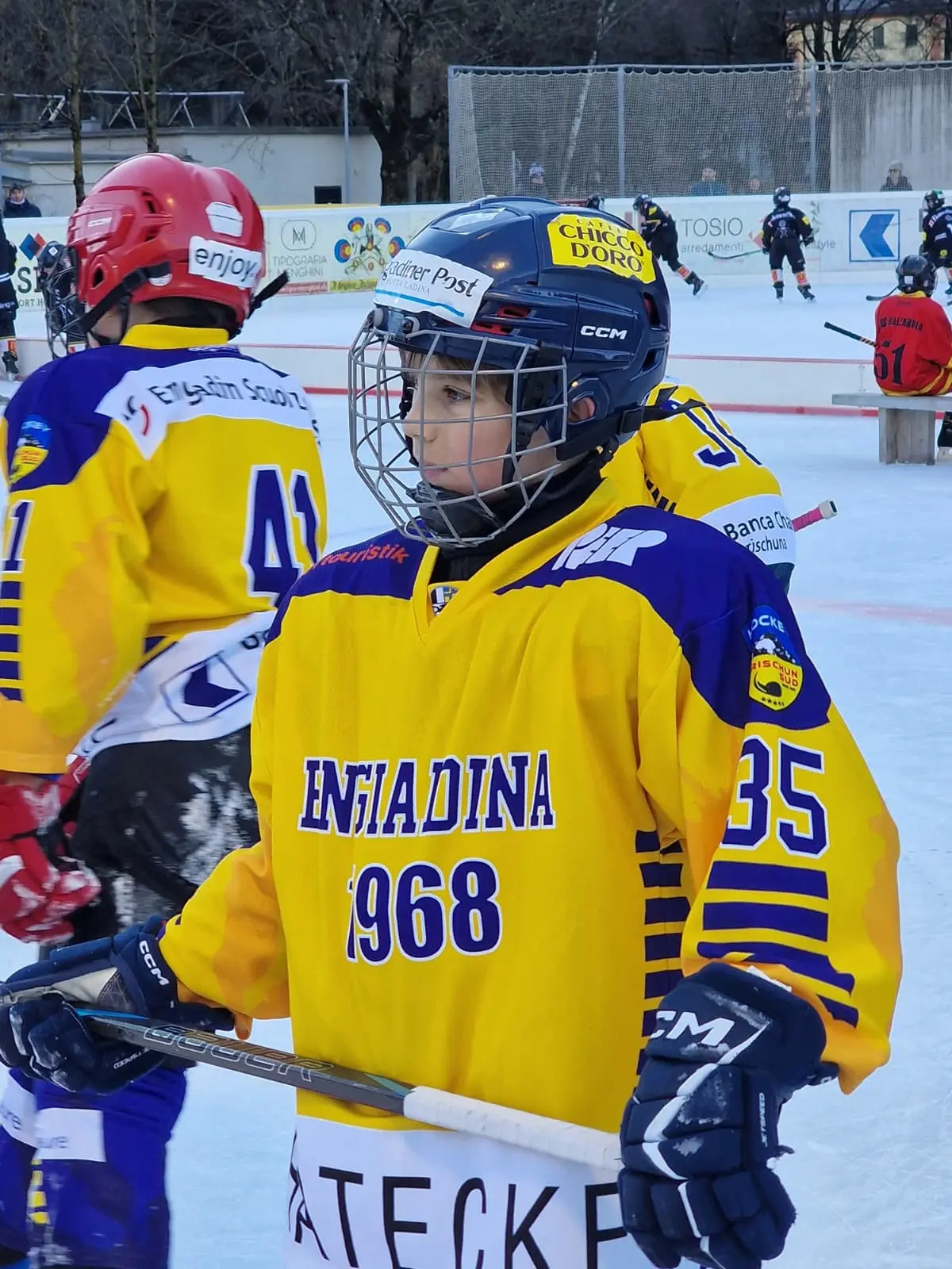 Giocatore di hockey su ghiaccio in uniforme gialla con il numero 35, mentre tiene la sua stecca. Sullo sfondo si vedono altri giocatori in azione.