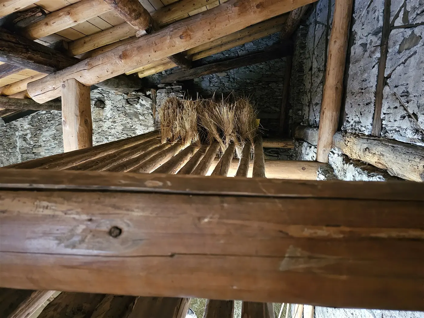 Interno di un fienile con travi di legno e un mucchio di fieno posizionato su un ripiano. La luce entra dall'alto, illuminando l'ambiente rustico.